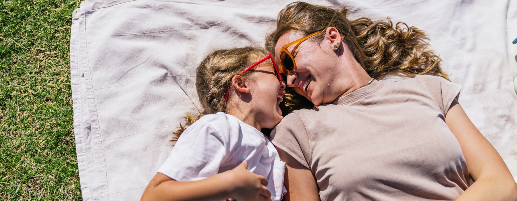Mother and daughter smiling and laughing on a picnic blanket in a park