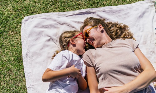 Mother and daughter smiling and laughing on a picnic blanket in a park